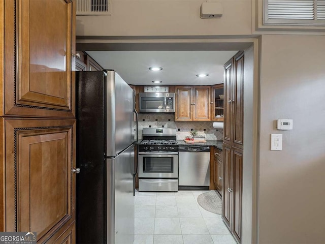 kitchen with light tile patterned floors, glass insert cabinets, appliances with stainless steel finishes, brown cabinets, and backsplash