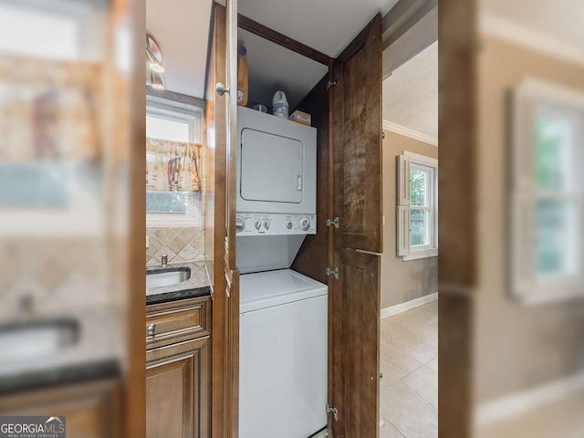 laundry room with baseboards, ornamental molding, stacked washer and dryer, laundry area, and a sink