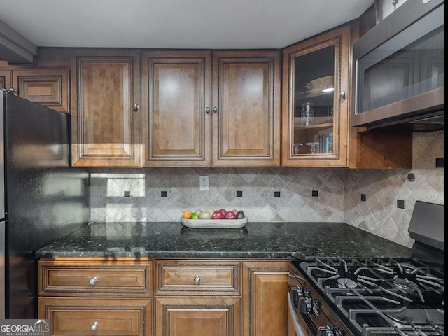 kitchen with tasteful backsplash, dark stone countertops, appliances with stainless steel finishes, and glass insert cabinets