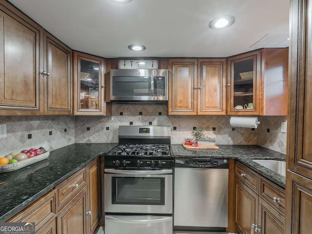 kitchen featuring brown cabinetry, decorative backsplash, stainless steel appliances, and dark stone counters