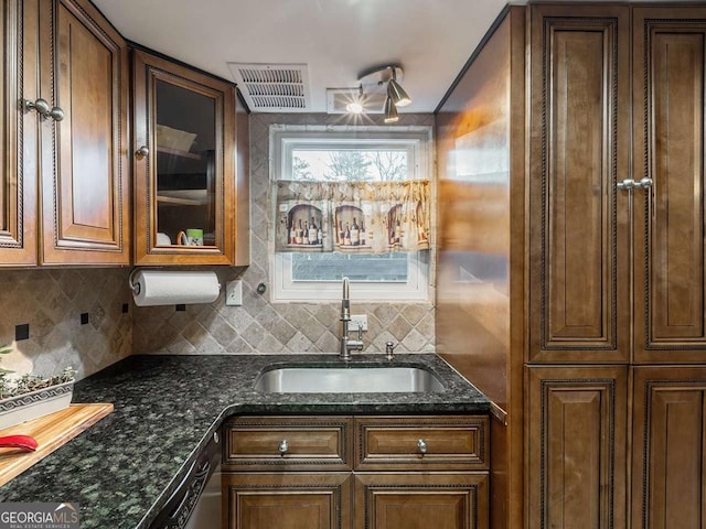 kitchen featuring visible vents, decorative backsplash, a sink, dark stone countertops, and glass insert cabinets