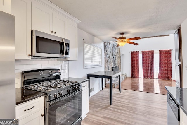 kitchen with appliances with stainless steel finishes, tasteful backsplash, white cabinets, a textured ceiling, and light hardwood / wood-style flooring