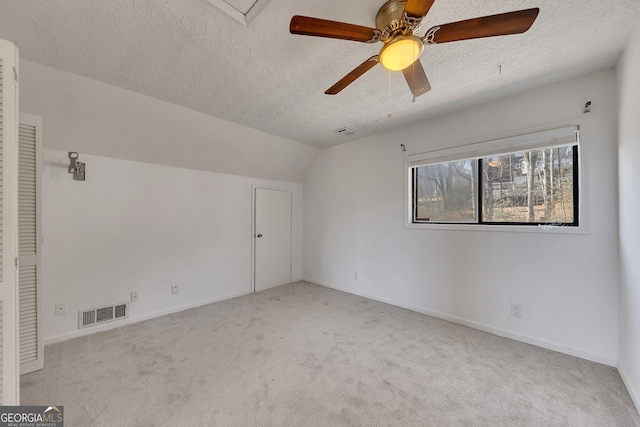 empty room featuring ceiling fan, light colored carpet, lofted ceiling, and a textured ceiling