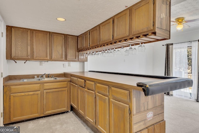 kitchen featuring sink, ceiling fan, kitchen peninsula, light carpet, and a textured ceiling