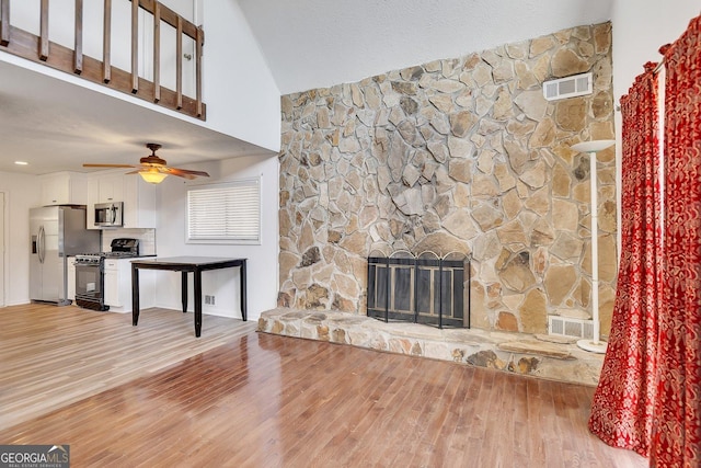 living room with ceiling fan, a stone fireplace, a textured ceiling, and light wood-type flooring