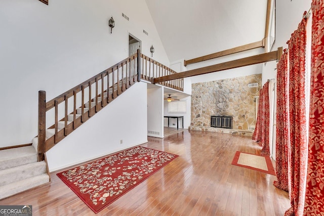 living room featuring hardwood / wood-style flooring, a towering ceiling, a fireplace, and ceiling fan