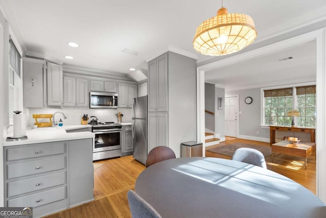 kitchen featuring hanging light fixtures, crown molding, gray cabinets, and stainless steel appliances