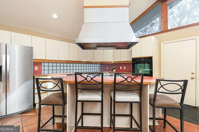 kitchen with black oven, a breakfast bar, white cabinetry, stainless steel refrigerator with ice dispenser, and island exhaust hood