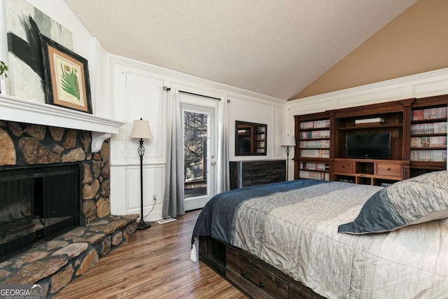 bedroom featuring lofted ceiling, a stone fireplace, a textured ceiling, access to outside, and hardwood / wood-style floors