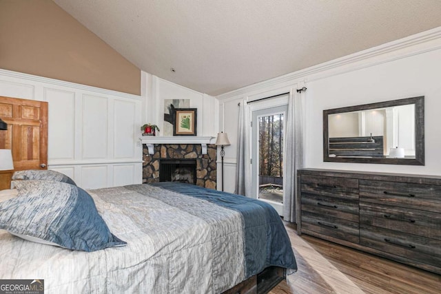 bedroom with a stone fireplace, lofted ceiling, access to exterior, light wood-type flooring, and a closet