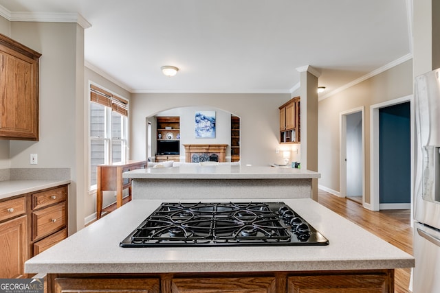 kitchen with stainless steel refrigerator with ice dispenser, crown molding, light wood-type flooring, a kitchen island, and black gas stovetop