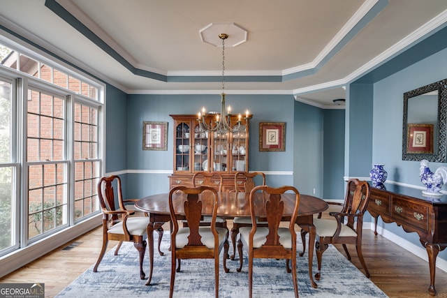 dining space with an inviting chandelier, a tray ceiling, crown molding, and hardwood / wood-style flooring