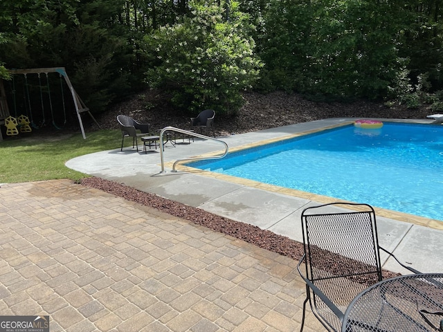 view of swimming pool with a playground, a patio area, and a diving board