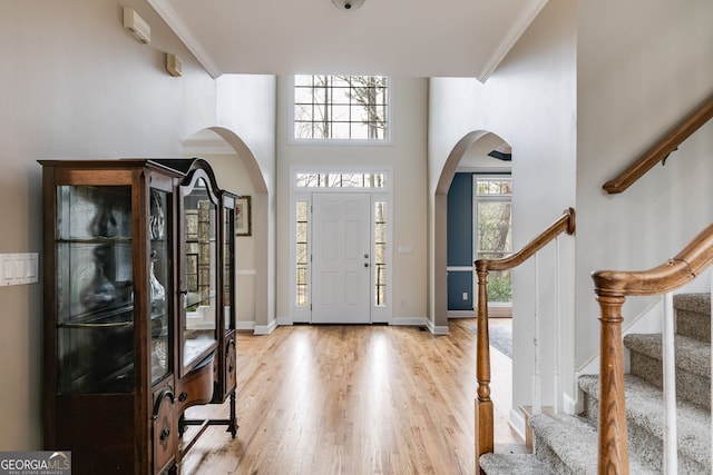 foyer featuring crown molding, a towering ceiling, and light wood-type flooring