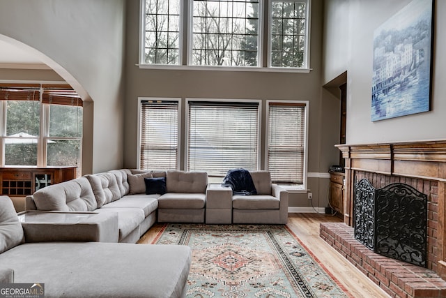 living room with a towering ceiling, a fireplace, light hardwood / wood-style floors, and a healthy amount of sunlight