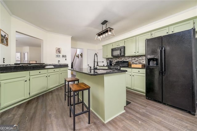 kitchen featuring green cabinets, a center island with sink, and black appliances