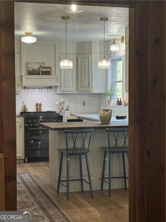 kitchen with a breakfast bar area, black range with gas stovetop, wood finished floors, and decorative backsplash