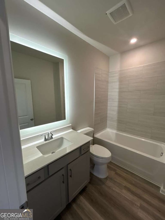 full bathroom featuring hardwood / wood-style flooring, vanity, tiled shower / bath combo, and toilet