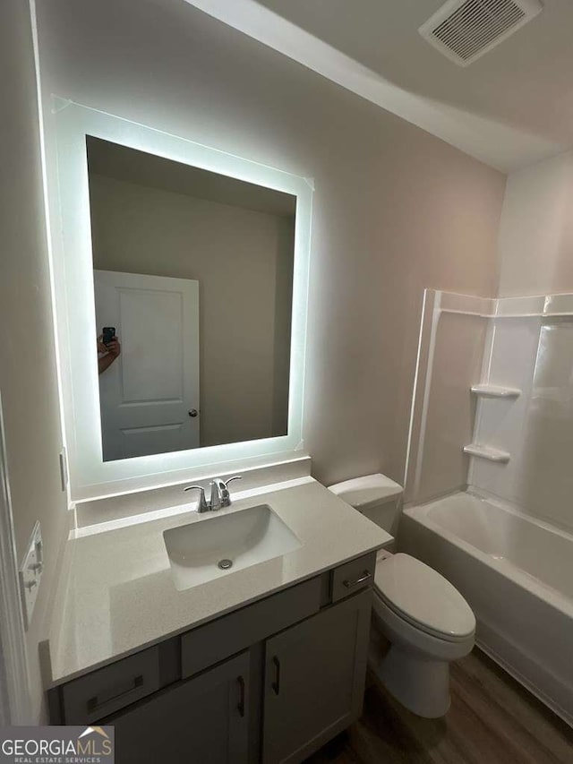 full bathroom featuring hardwood / wood-style flooring, vanity, shower / tub combination, and toilet