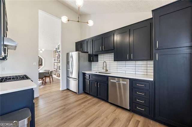 kitchen featuring appliances with stainless steel finishes, sink, decorative backsplash, wall chimney range hood, and light wood-type flooring