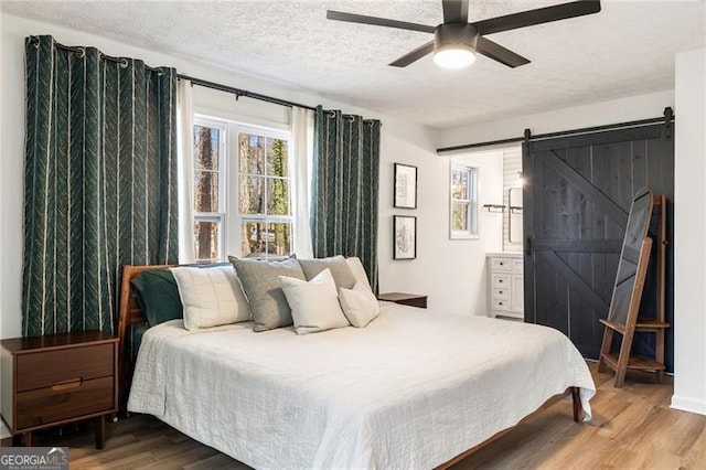 bedroom with hardwood / wood-style floors, a barn door, a textured ceiling, and ceiling fan