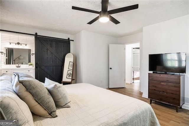 bedroom with hardwood / wood-style floors, sink, ceiling fan, a barn door, and a textured ceiling