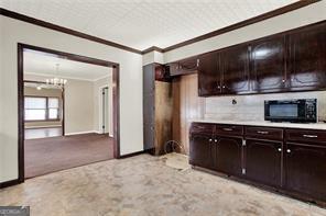 kitchen with black microwave, ornamental molding, light colored carpet, dark brown cabinetry, and an inviting chandelier