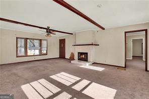 unfurnished living room featuring beamed ceiling, ceiling fan, and carpet