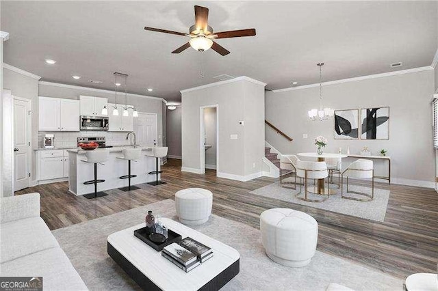 living room with crown molding, sink, ceiling fan with notable chandelier, and dark wood-type flooring