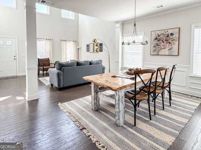 dining area featuring dark wood-type flooring, a chandelier, ornamental molding, decorative columns, and a high ceiling