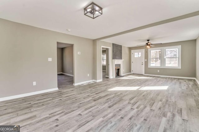 unfurnished living room with a brick fireplace, ceiling fan, and light wood-type flooring