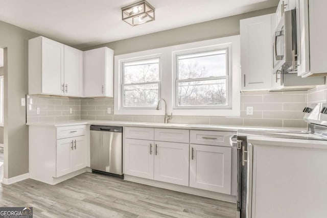 kitchen with sink, light hardwood / wood-style flooring, appliances with stainless steel finishes, backsplash, and white cabinets