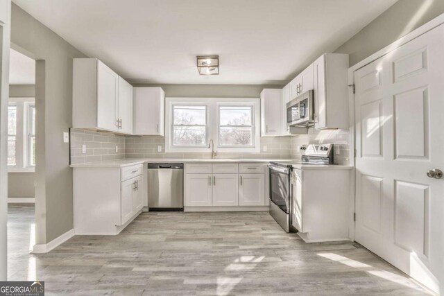 kitchen with backsplash, light wood-type flooring, white cabinets, and appliances with stainless steel finishes