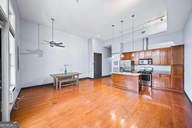 kitchen with hanging light fixtures, a center island with sink, a towering ceiling, stainless steel appliances, and hardwood / wood-style floors