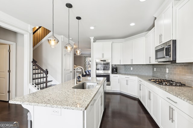 kitchen with sink, a kitchen island with sink, white cabinetry, stainless steel appliances, and light stone counters