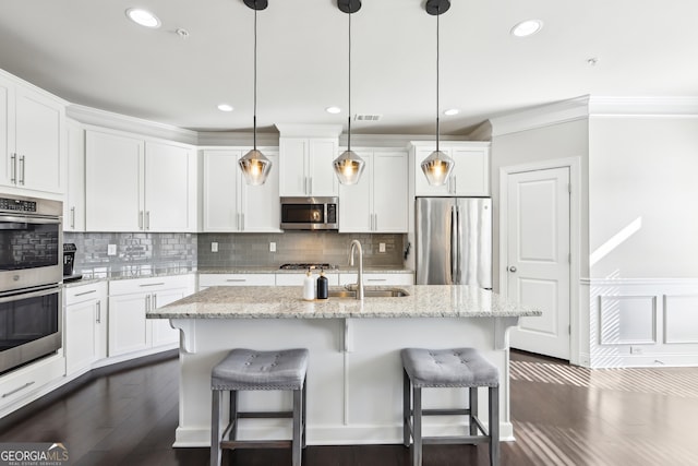 kitchen with an island with sink, white cabinetry, hanging light fixtures, light stone counters, and stainless steel appliances