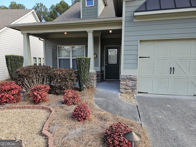 doorway to property with driveway, stone siding, a porch, and roof with shingles