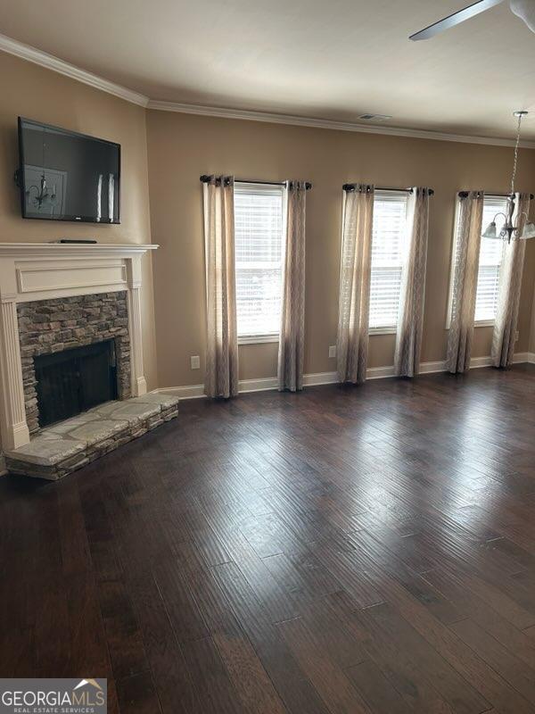 unfurnished living room with dark wood finished floors, crown molding, a stone fireplace, and baseboards