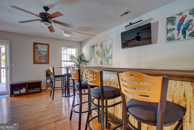 bar with ceiling fan, hardwood / wood-style flooring, a wealth of natural light, and a textured ceiling