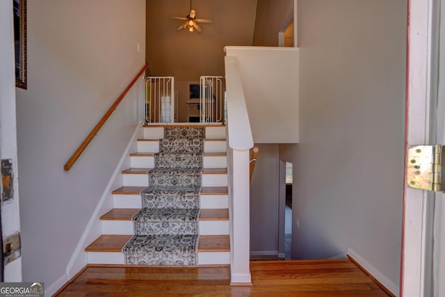 stairway featuring hardwood / wood-style flooring, a high ceiling, and ceiling fan