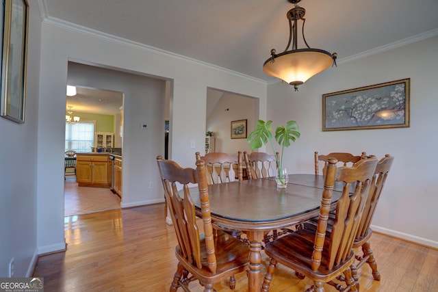 dining space with ornamental molding, a notable chandelier, and light hardwood / wood-style floors