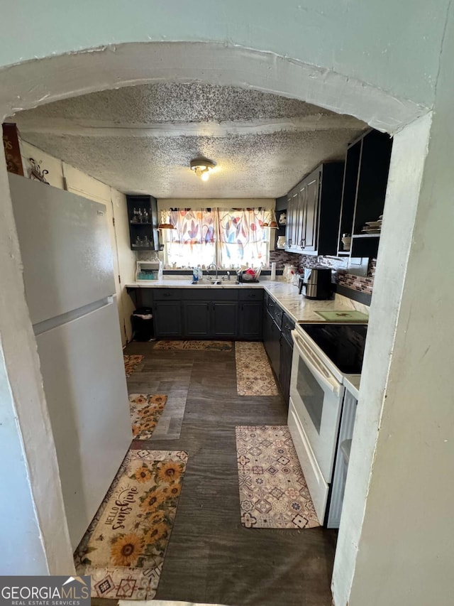 kitchen featuring dark wood-type flooring, white appliances, sink, and a textured ceiling