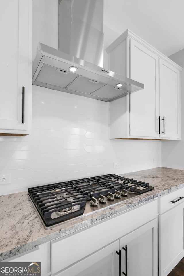 39 Pecan Ct, Hoschton, GA 30548 - kitchen with wall chimney range hood, stainless steel gas cooktop, backsplash, white cabinetry, and light stone countertops