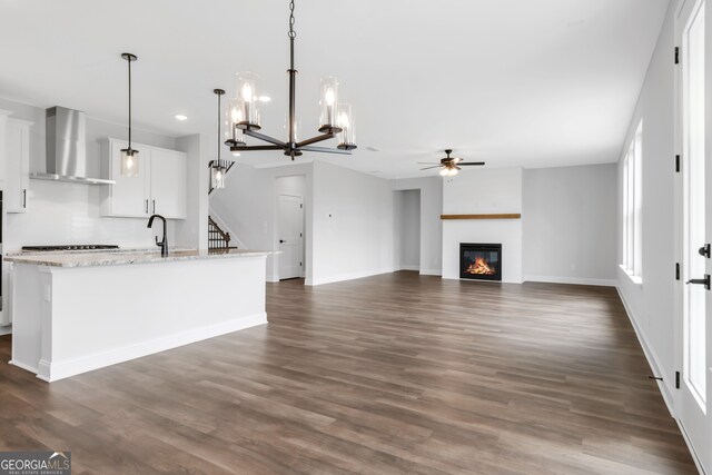 39 Pecan Ct, Hoschton, GA 30548 - kitchen featuring wall chimney range hood, ceiling fan, white cabinetry, stovetop, and a glass covered fireplace