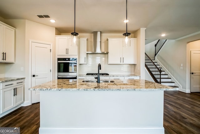 kitchen with wall chimney exhaust hood, sink, white cabinetry, an island with sink, and pendant lighting