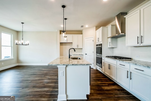 kitchen featuring an island with sink, sink, wall chimney range hood, and white cabinets