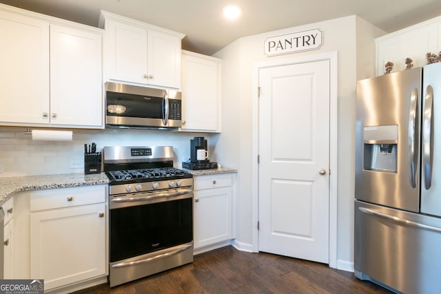 kitchen with appliances with stainless steel finishes, white cabinets, dark hardwood / wood-style flooring, decorative backsplash, and light stone countertops