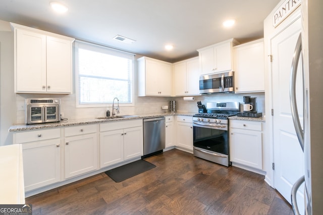 kitchen featuring sink, dark wood-type flooring, appliances with stainless steel finishes, white cabinetry, and light stone counters