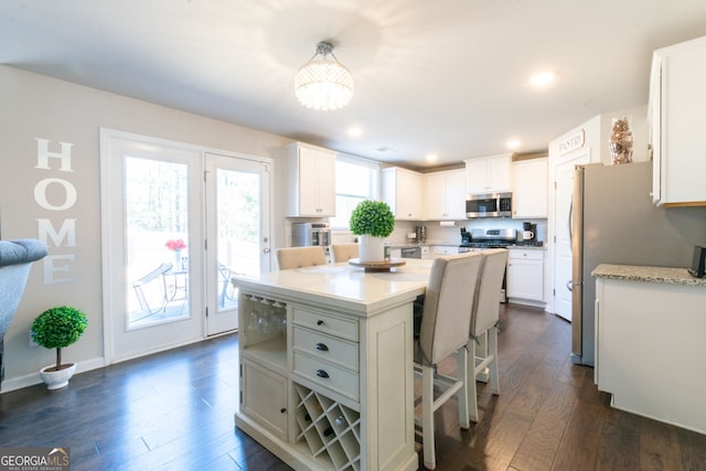 kitchen featuring pendant lighting, dark wood-type flooring, appliances with stainless steel finishes, white cabinetry, and a kitchen island