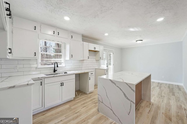 kitchen featuring sink, a center island, light wood-type flooring, white cabinets, and backsplash